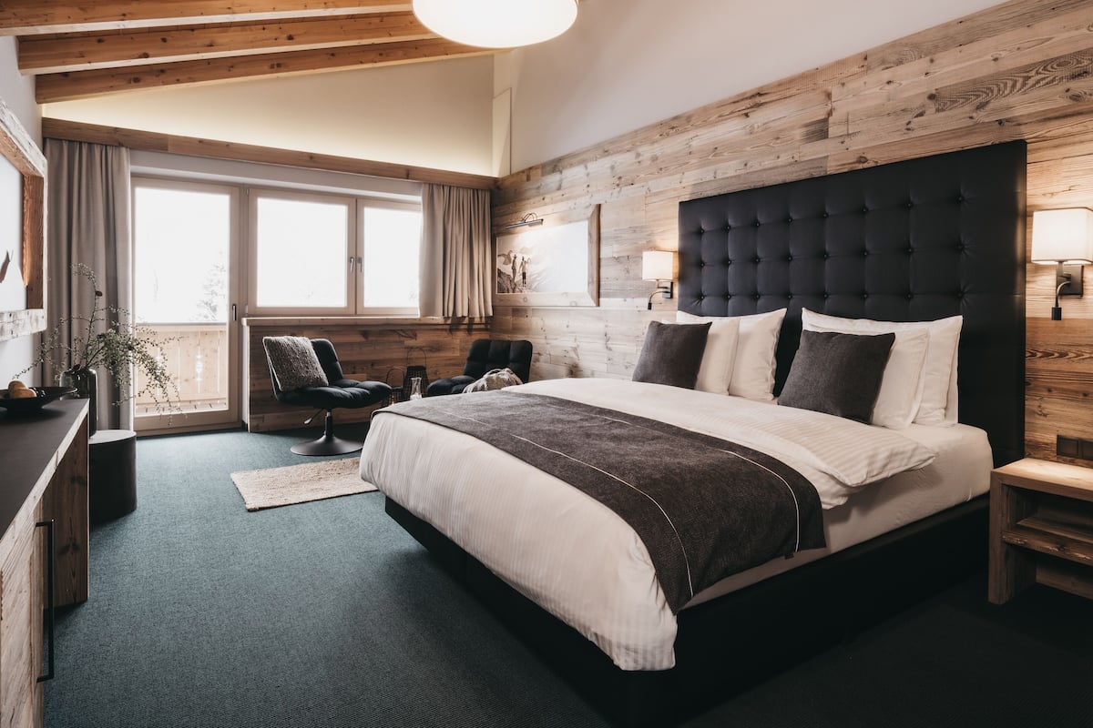 Een slaapkamer met een groot bed, houten wanden, een raam en een stoel.
