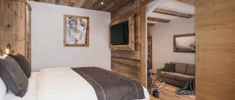 Un dormitorio con techo de madera, una cama con ropa de cama blanca y marrón, un televisor montado y un armario de madera.