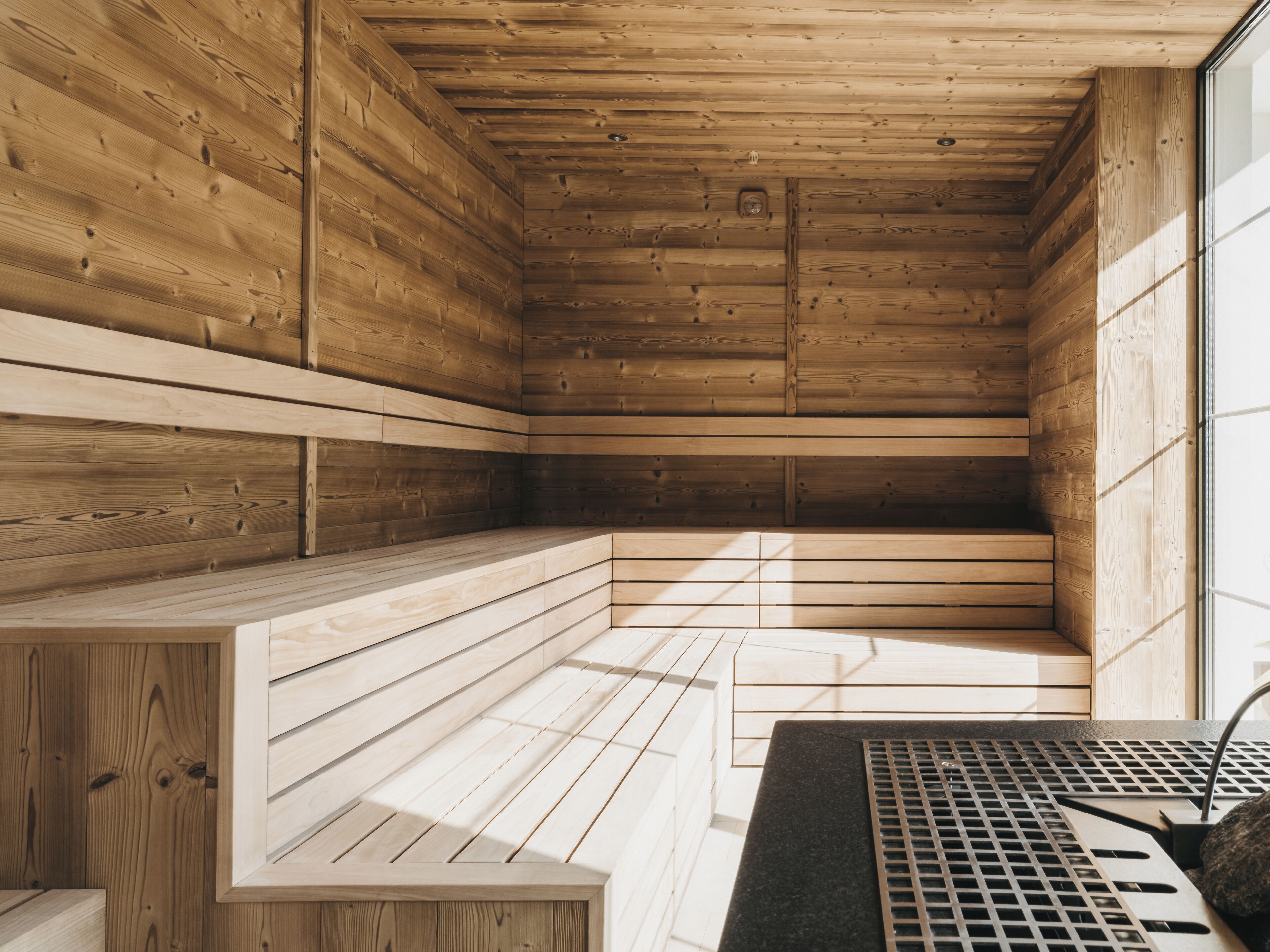 A sauna with wooden walls and benches, a metal grate, and a window for natural light.