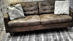 Une pièce avec un canapé en cuir marron placé contre un mur gris texturé, un lampadaire et un plancher en bois à carreaux.