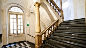 Un escalier avec un sol à carreaux, une main courante et une fenêtre à motifs géométriques.
