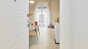 Hotelkamer met een witte deur, een eethoek met een tafel en stoelen, een witte wasmachine en uitzicht op het balkon.