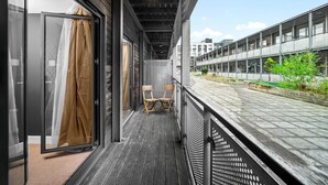 Balcón con vista a un tren y edificios, con una silla de madera y un vidrio con cortina.