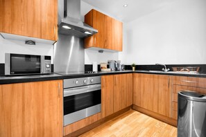 A modern kitchen with stainless steel appliances, wooden cabinets, and a black countertop.