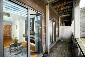 Un intérieur moderne avec une porte vitrée donnant sur un balcon, une petite table agrémentée d’une plante et un plancher en bois.
