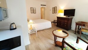 A hotel room with a bed, bedside table with lamp, TV, wooden dresser, and a small round table. - Appart'hotel Le Saint Antoine - Le Studio Confort en Centre Ville (Albi)