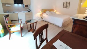 A compact hotel room with a bed, a small desk, a chair, a round table, a microwave, a kettle, and a sink. - Appart'hotel Le Saint Antoine - Le Studio Confort en Centre Ville (Albi)