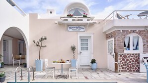 A poolside area with a dining setup, a sign for Meroviglioso Apartments - Studios, and a stone wall. - Merovigliosso Budget Studio ground floor (Thira - Santorini)