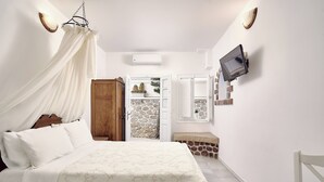 A bedroom with a bed, a wooden wardrobe, a stone wall, a television mounted on the wall, and a bench. - Merovigliosso Budget Studio ground floor (Thira - Santorini)