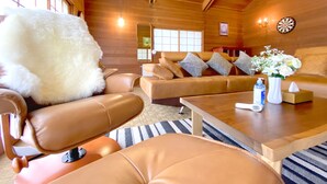 Una sala de estar acogedora con muebles de cuero, un sillón blanco mullido, un jarrón con flores y un dardo en la pared.