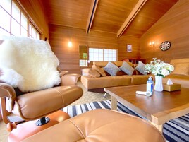 Una sala de estar acogedora con muebles de cuero, un sillón blanco mullido, un jarrón con flores y un dardo en la pared.