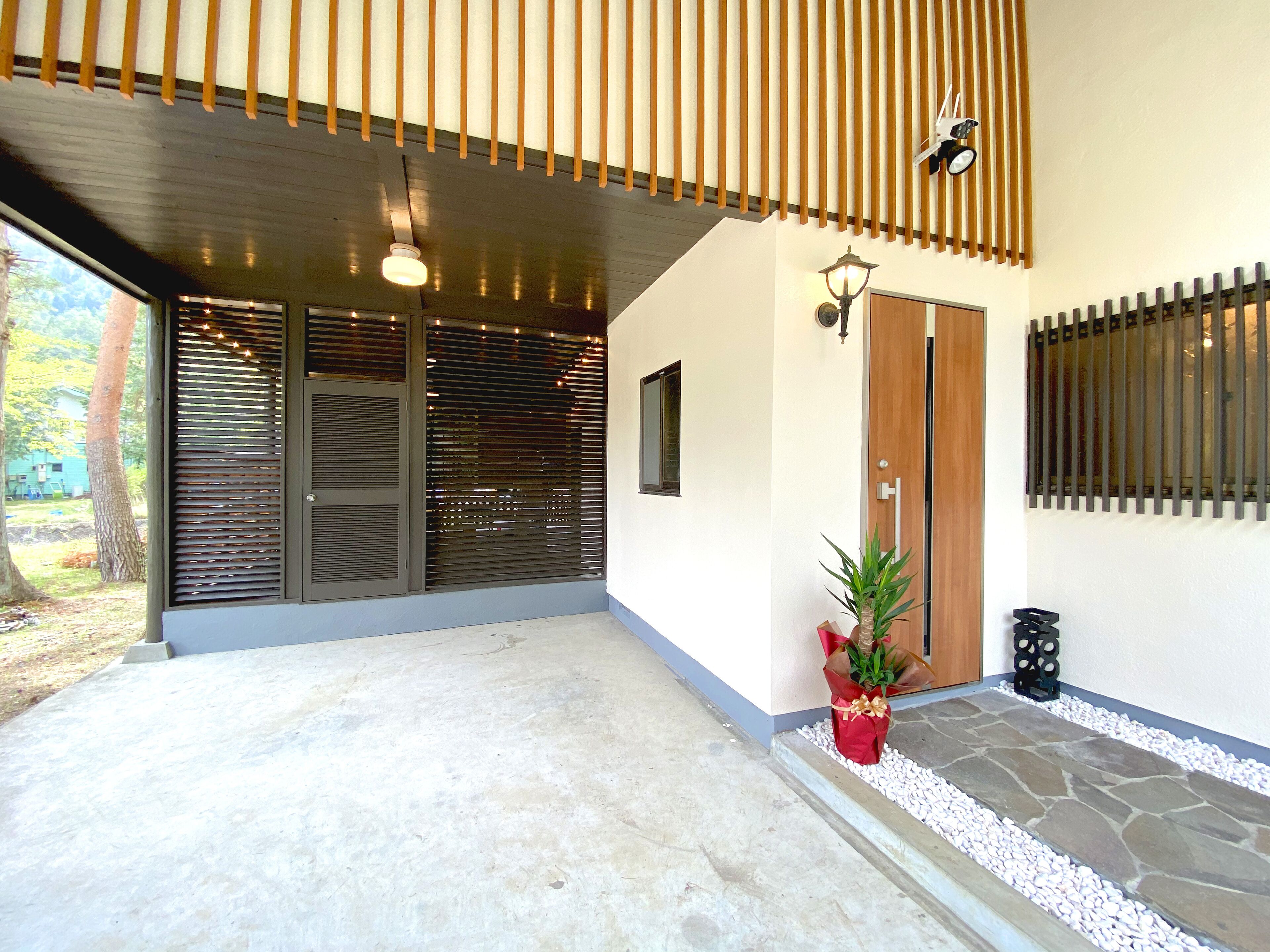 Ingresso moderno di un edificio con un portico coperto, una pianta in vaso e un vialetto in pietra che conduce alla porta.