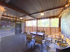 Un espacio de estar techado al aire libre con un suelo de madera, una mesa con sillas y luces colgantes.