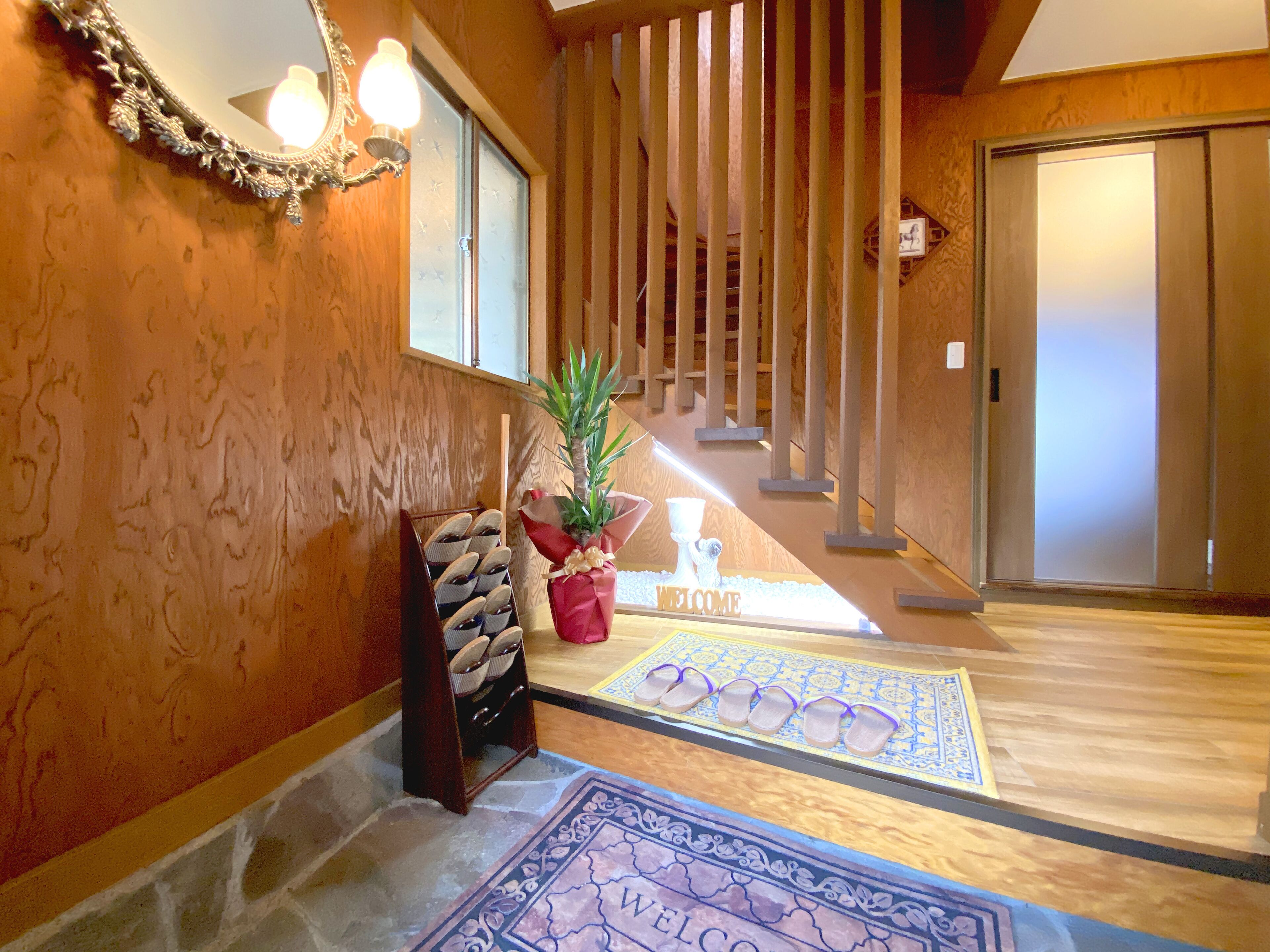 A wooden interior with a staircase, a welcome mat, and a shoe rack.