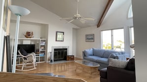 Ein geräumiges Wohnzimmer mit Kamin, Deckenventilator, großem Fenster und Fernseher.