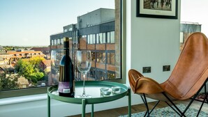 A modern room with a large window, a brown leather chair, a small table with a bottle and glass, and a framed picture on the wall. - Cityscape @ Ryedale House -  a family break that sleeps 4 guests  in 2 bedrooms (York)