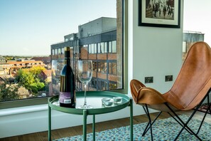 A modern room with a large window, a brown leather chair, a small table with a bottle and glass, and a framed picture on the wall. - Cityscape @ Ryedale House -  a family break that sleeps 4 guests  in 2 bedrooms (York)