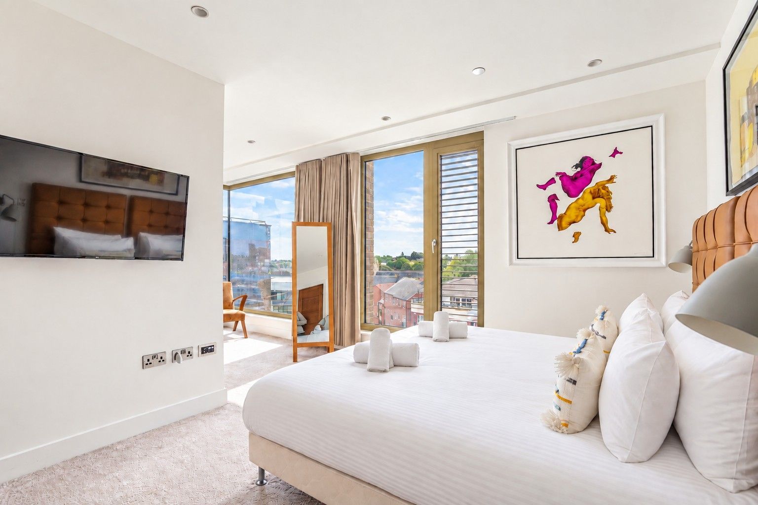 Ein modernes Hotelzimmer mit einem großen Bett, einem Flachbildfernseher, Blick auf die Stadt und einem gerahmten Kunstwerk.