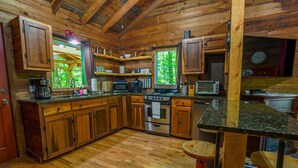 Cocina de cabaña de madera con una isla grande, electrodomésticos integrados y vistas al exterior con vegetación.