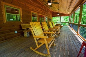 A wooden cabin with a porch featuring rocking chairs and a ceiling fan.