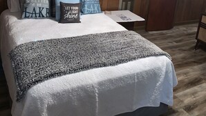 Ein Schlafzimmer mit Holzboden, einem Bett mit vielen Kissen, einem Deckenventilator, einem Nachttisch und einer Tür.