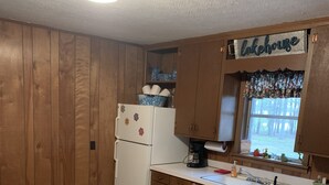 Eine kompakte Küche mit Holzausstattung, einem weißen Kühlschrank, einem Esstisch mit Stühlen und einem Fenster mit Blick ins Freie.