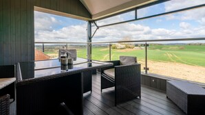 A covered outdoor seating area with a glass table and wicker chairs, overlooking a green landscape. - Lower Lodge Barn - sleeps 8 guests  in 4 bedrooms (Alcester)