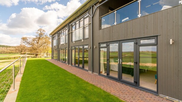 A modern building with large windows and a grassy area in front. - Lower Lodge Barn - sleeps 8 guests  in 4 bedrooms (Alcester)