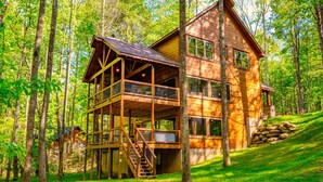 A two-story wooden cabin with a balcony and a staircase, surrounded by a forest. - Luxury, Cozy & Fun ★ Pool, Hot Tub, Theater, Games (Sevierville)