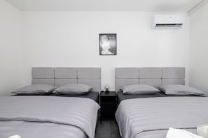 Ein Doppelzimmer mit zwei Betten, einem Nachttisch, einer Lampe und einer Wand-Klimaanlage.