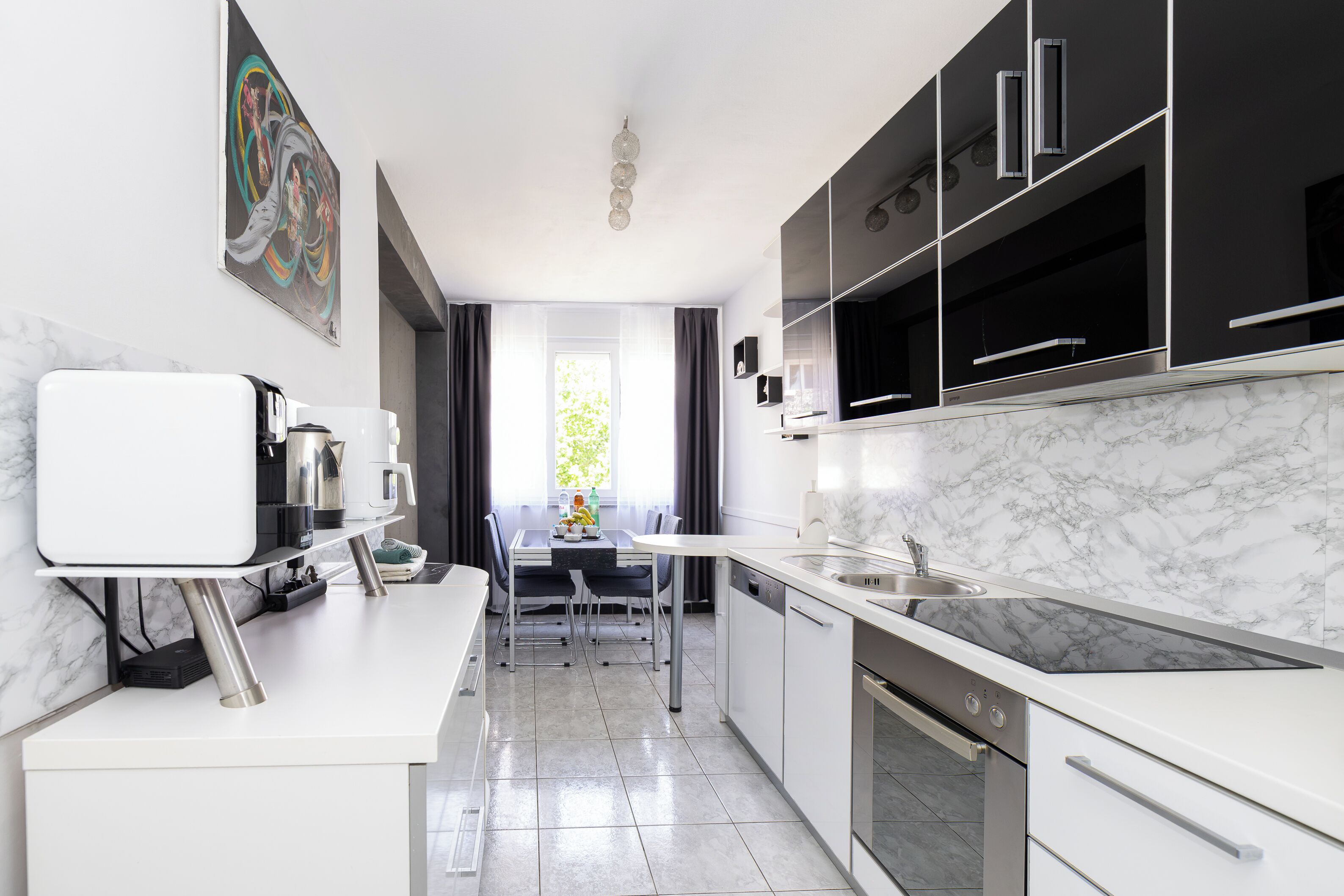 Une cuisine moderne avec des plans de travail blancs, un four encastré et un coin repas comprenant une table et des chaises.
