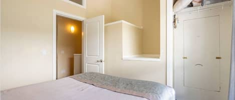 Une chambre d’hôtel avec un lit, une armoire, une porte et une petite fenêtre.