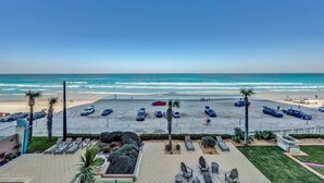 A beach view from a hotel balcony with a parking area, lounge chairs, and a clear sky. - WOW! Gorgeous Oceanfront Luxury Condo (Daytona Beach)