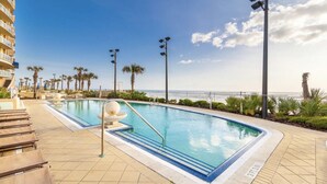 A swimming pool with lounge chairs, palm trees, and a view of the ocean. - WOW! Gorgeous Oceanfront Luxury Condo (Daytona Beach)