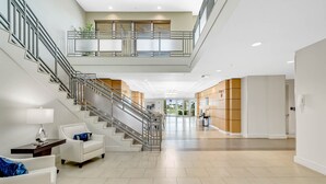 A spacious lobby with a staircase, a seating area with a table and chairs, and a view of the upper floor. - WOW! Gorgeous Oceanfront Luxury Condo (Daytona Beach)