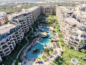 Ein mehrstöckiges Hotel mit einem zentral gelegenen Schwimmbecken, umgeben von Liegestühlen und Palmen.
