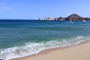 Ein Strand mit klarem, blauem Wasser, einem sandigen Ufer und Felsformationen in der Ferne.