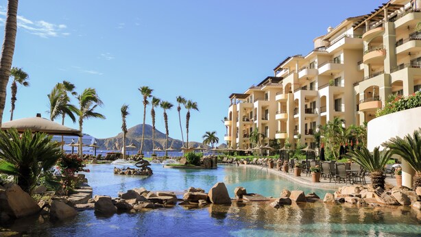 Ein Pool in einem Resort mit Felsen, Palmen und einem Berg im Hintergrund.
