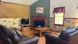 A living room with a fireplace, leather sofas, a wooden coffee table, and a television on a wooden stand. - Patoka Lake Deluxe with Jacuzzi #17 at Patoka 4 Seasons Resort (Eckerty)