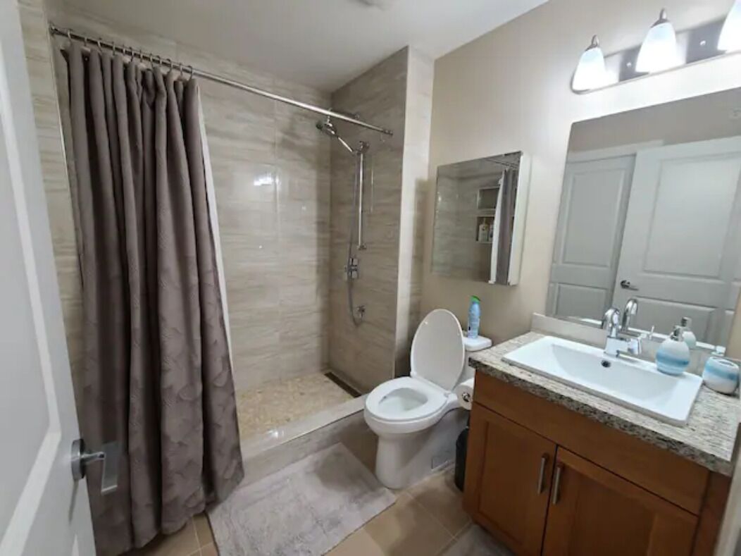 A bathroom with a shower, toilet, sink, and mirror.