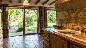 Ein Badezimmer mit einem großen Waschbecken, Holzschränken und Blick auf einen Garten durch eine Schiebeglastür.