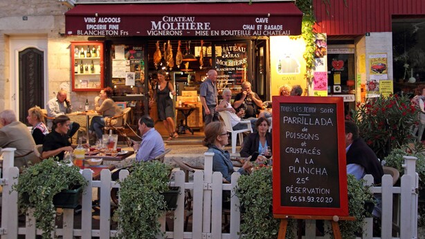 Ein Restaurant mit Außenbereich, einem Schild, das 'Parrillada de Poissons et Crustacés' bewirbt, und einem roten Markisenvorzelt mit der Aufschrift 'Chateau Molhieres'.