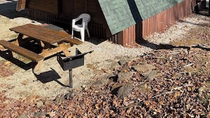 A small, rustic cabin with a sloped green roof, a wooden door, and a picnic table outside.
