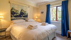 A neatly made bed with folded towels, a painting on the wall, and a window with curtains. - Tree Tops at The Falls -  3-bedroom duplex, stroll into Ambleside (Ambleside)
