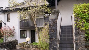 A stone-walled building with a balcony, a door, and a small garden area with a tree and a lamp post. - Tree Tops at The Falls -  3-bedroom duplex, stroll into Ambleside (Ambleside)