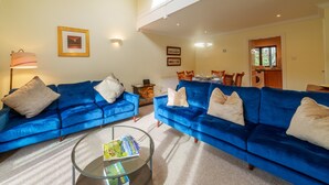 A living room with two blue sofas, a glass coffee table, and a dining area with chairs and a table. - Tree Tops at The Falls -  3-bedroom duplex, stroll into Ambleside (Ambleside)