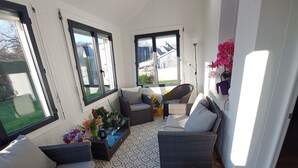 A sunlit room with wicker furniture, a patterned rug, and large windows offering a view of the outdoors. - House located in Concarneau in a quiet area close to amenities (Concarneau)