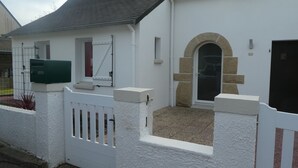 A white building with a stone archway entrance, a white picket fence, and a green mailbox. - House located in Concarneau in a quiet area close to amenities (Concarneau)