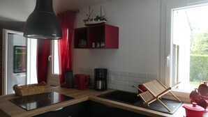 A kitchen with a black pendant light, red curtains, a small shelf with jars, a coffee maker, and a red pot. - House located in Concarneau in a quiet area close to amenities (Concarneau)