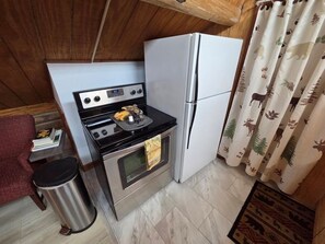 Eine kleine Küche mit Herd, Backofen und Kühlschrank, einem Mülleimer und einem Vorhang mit Tiermotiven.
